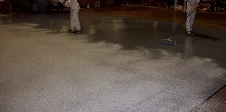 Non-slip flooring—workers spreading textured floor coating to create a slip-resistant surface in an industrial space.