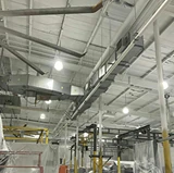 Industrial facility ceiling being painted, with exposed beams, ductwork, and bright overhead lighting.