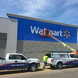 Workers on a lift painting the exterior of a Walmart building, with branded trucks parked in front.