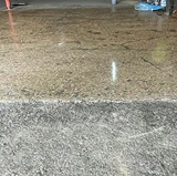 Concrete floor partially resurfaced, showing rough, worn concrete transitioning into a polished, repaired section with a glossy finish.