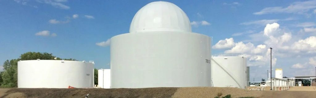 Large white storage tanks, including a central domed tank, under a blue sky.
