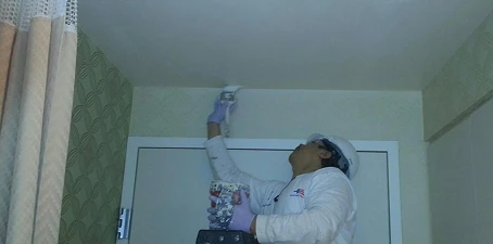 Hospitality hotel painting—worker applying paint to a ceiling corner inside a medical building.