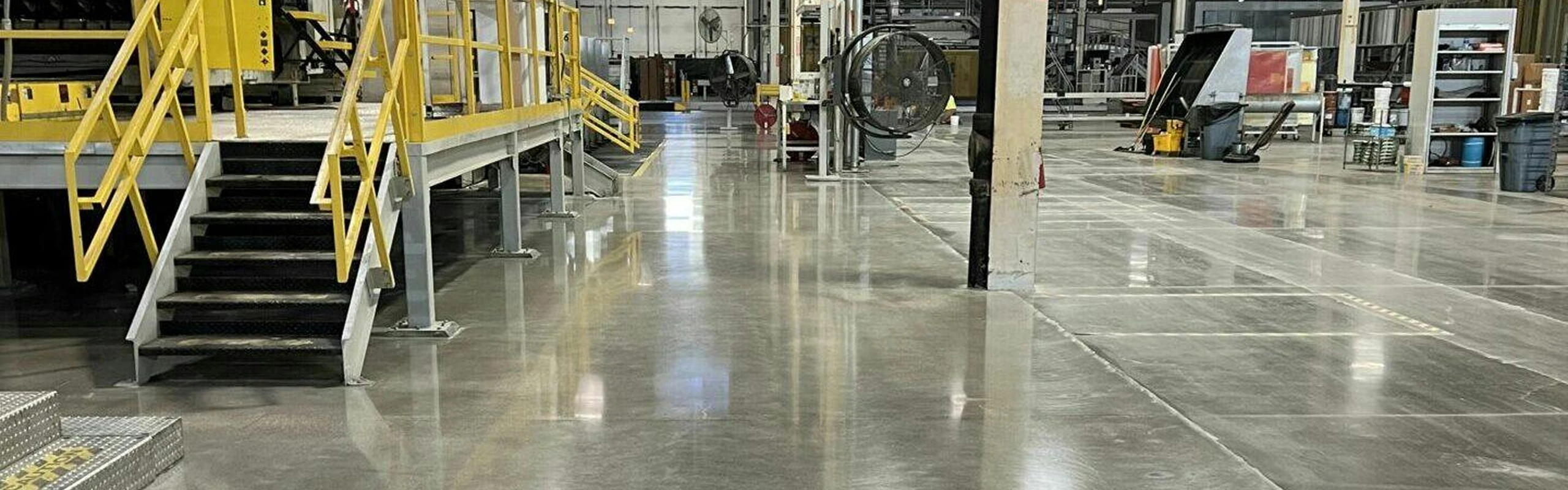 Polished concrete floor in a manufacturing plant with yellow-railed platforms, stairs, and machinery lining wide aisles.
